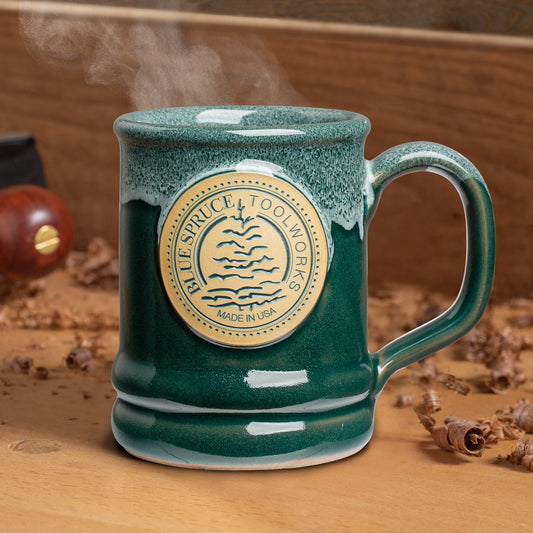 The Blue Spruce 2025 Signature Mug sitting upon a workbench. 