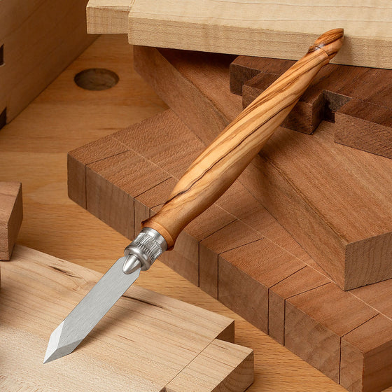 The Limited-Edition Blue Spruce Classic Marking Knife with Olivewood handle resting among resting among a variety of dovetail, box, and other joinery.