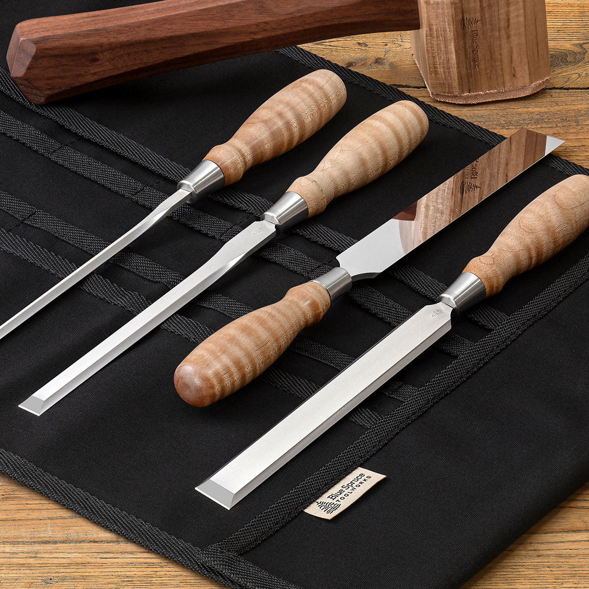 Set of Blue Spruce Paring Chisels with Resin-Infused Curly Maple handles resting on a Blue Spruce Canvas Tool Roll (sold separately).