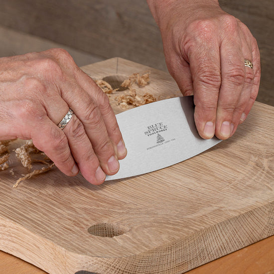 Person using a knife with card scraper on a wooden surface