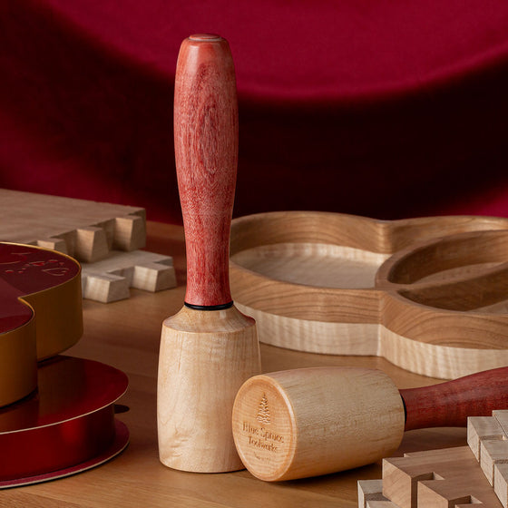 Two Blue Spruce Sweetheart Mallets displayed on a workbench, surrounded by heart-shaped chocolate boxes, and heart-shaped wood dish, and dovetailed boards.